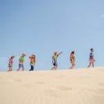 Low angle side view of unrecognizable people in colorful summer clothes walking on sandy beach against cloudless blue sky on sunny day